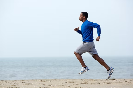 Man jogging on beach with ocean in background.