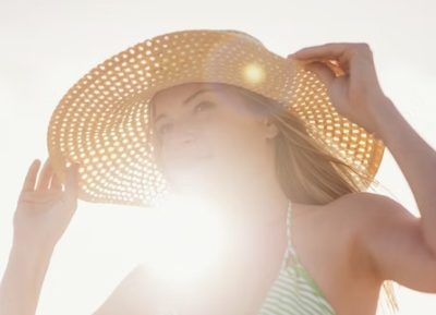Woman in straw hat and bikini, shielding eyes from bright sunlight.
