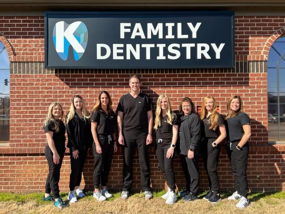the family dentistry team is posing for a picture in front of a brick building .