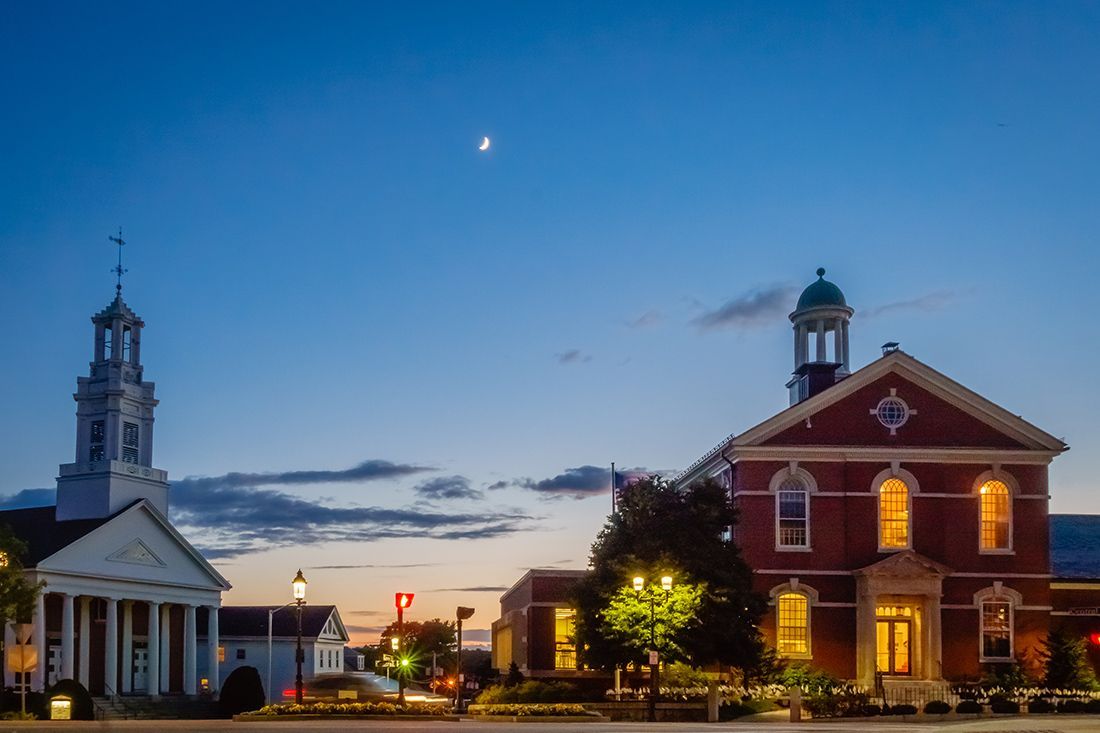 A city at night with a clock tower and a courthouse.