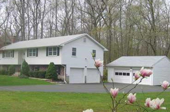 A white house with a garage next to it and flowers in front of it.