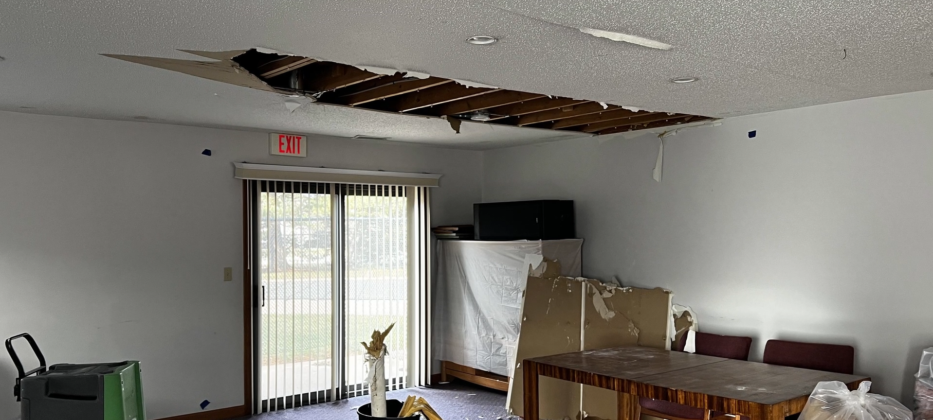 A living room with a hole in the ceiling and a sliding glass door.