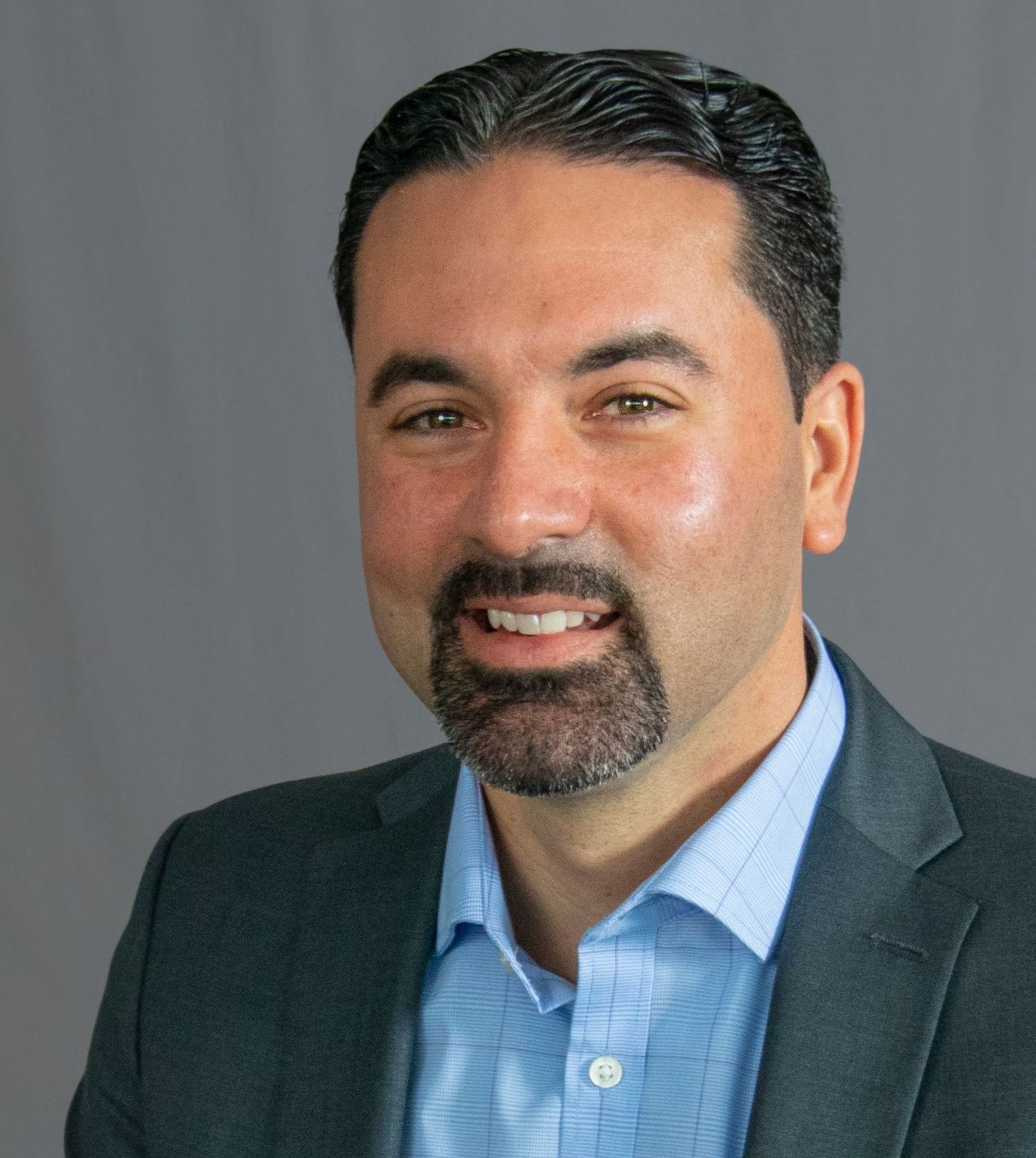 A man with a beard is wearing a suit and a blue shirt.