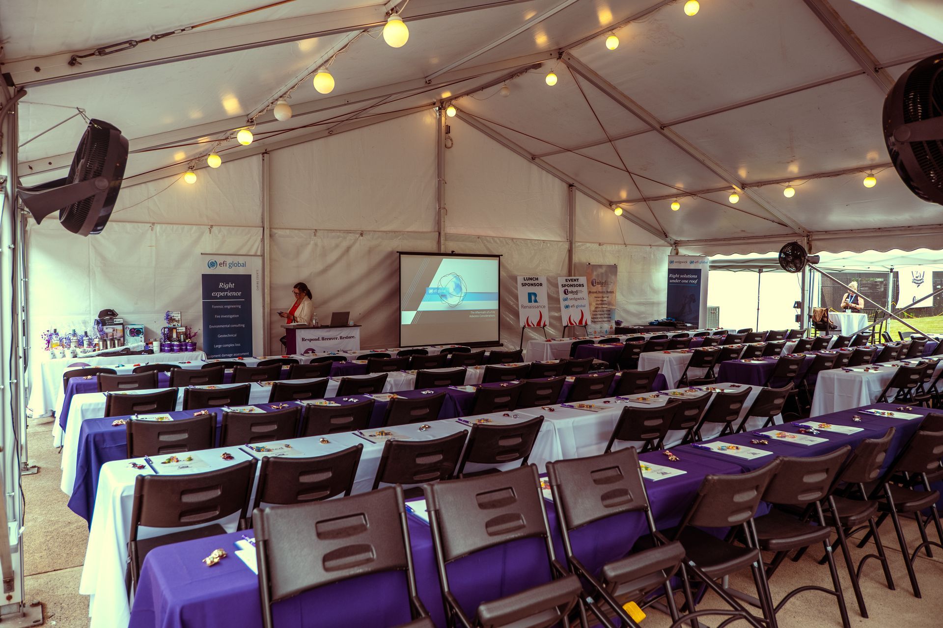 A large tent with tables and chairs and a projector screen