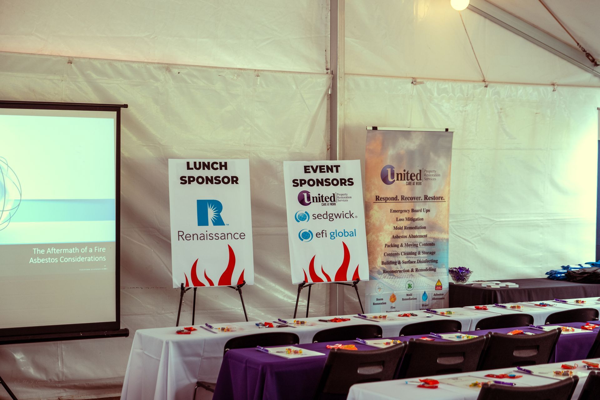 A white tent with tables and chairs and a projector screen