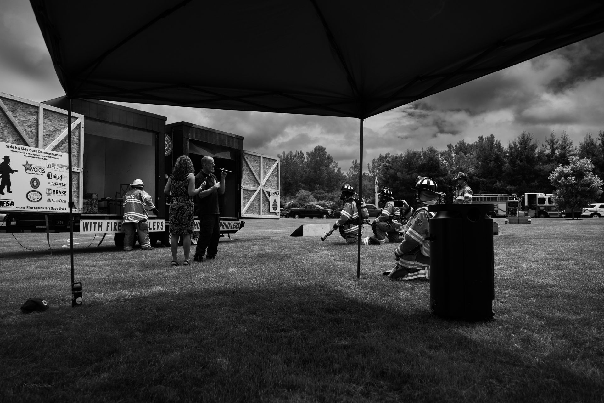 A black and white photo of a group of people standing under a tent in a field.