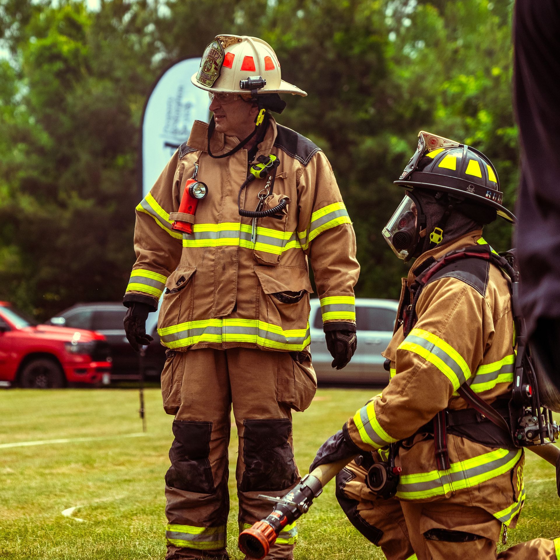 Two firefighters are standing in a field talking to each other