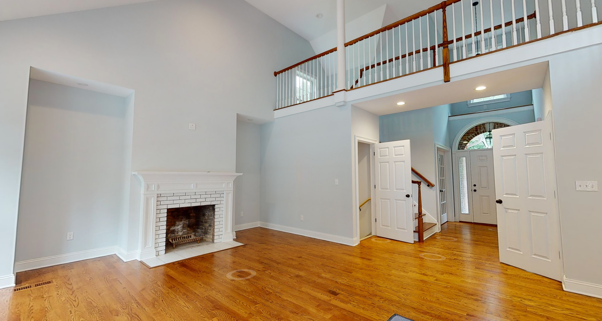 Spacious living room with a fireplace, hardwood floors, and a balcony overlooking the entry.
