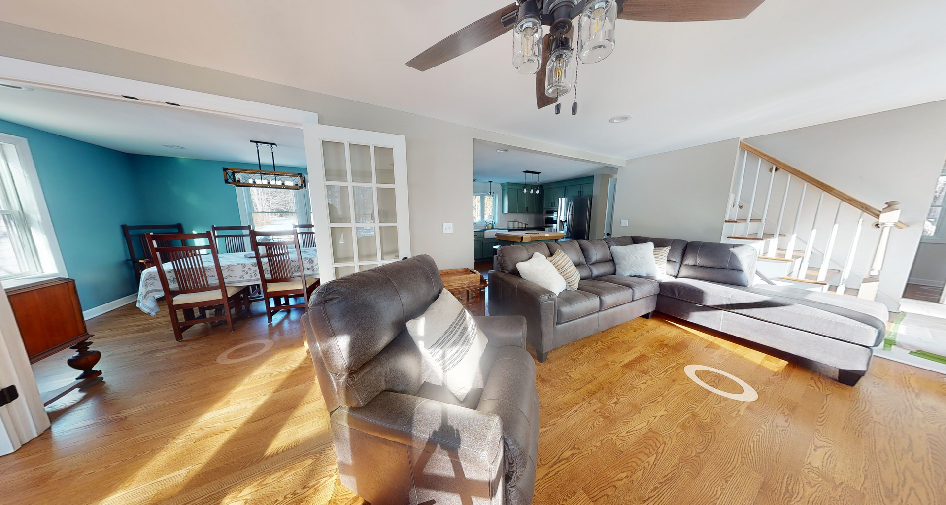 Panoramic view of a living room with hardwood floors, a sectional sofa, and a dining area visible through a doorway.