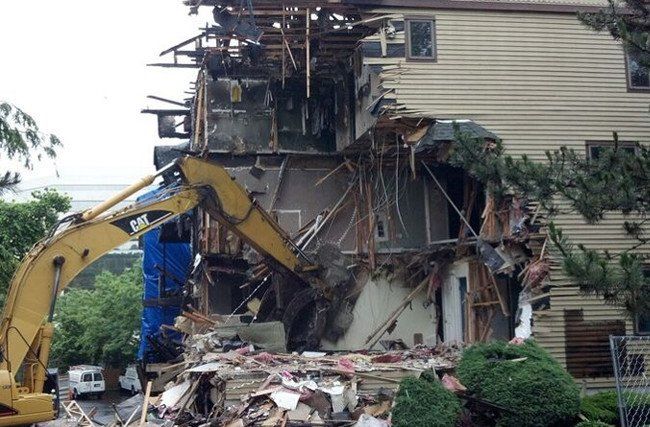 A large building is being demolished by a yellow excavator.
