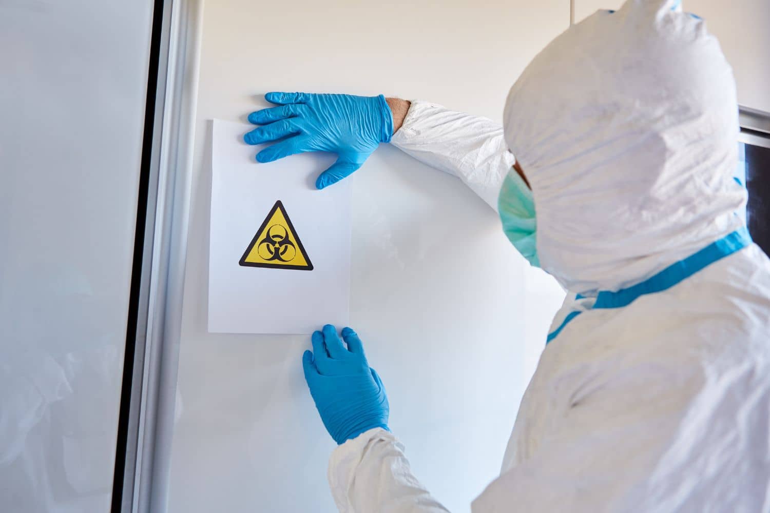 A person in a protective suit is holding a sign on a wall.