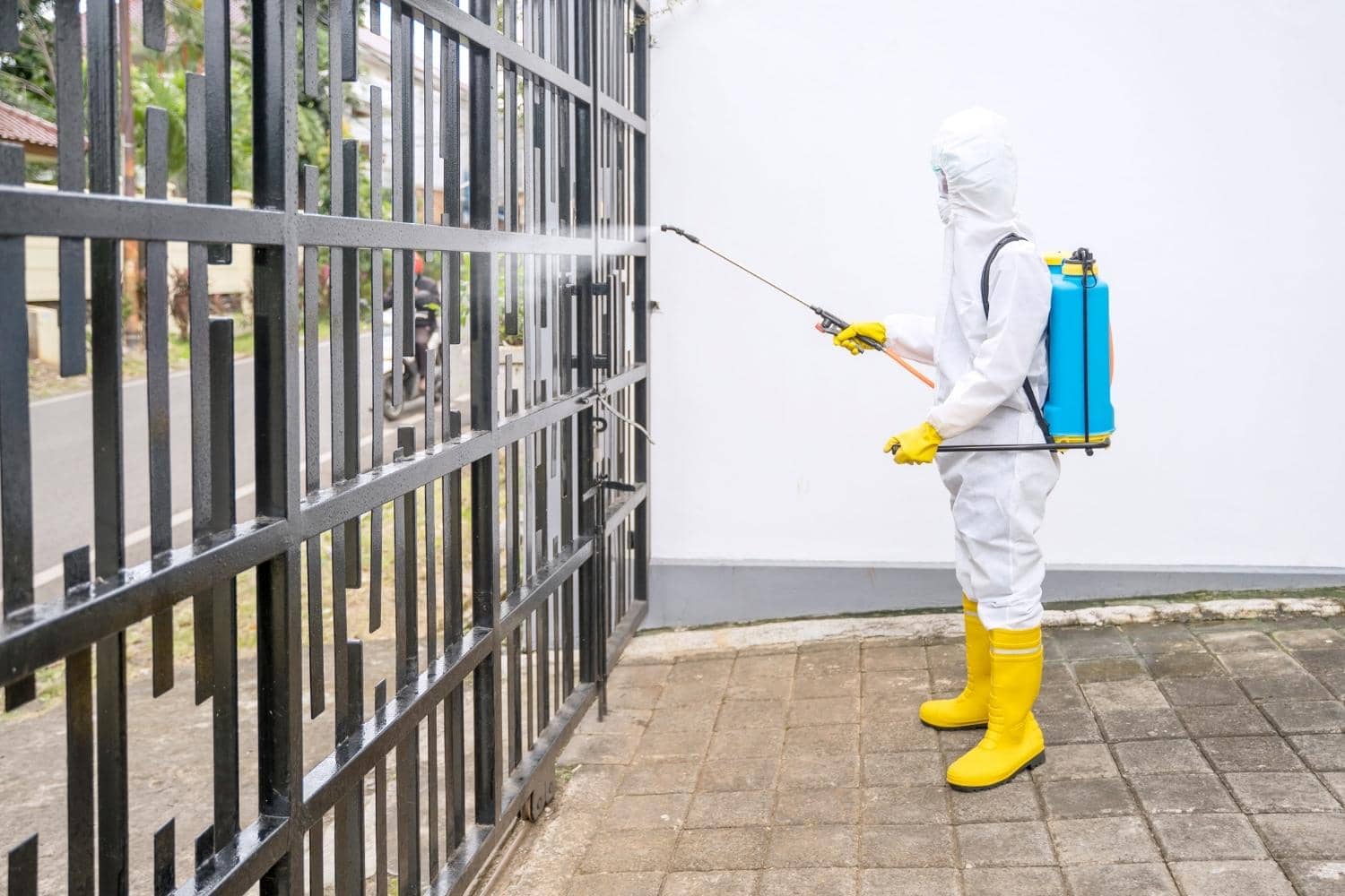 A man in a protective suit is spraying a fence with a sprayer.