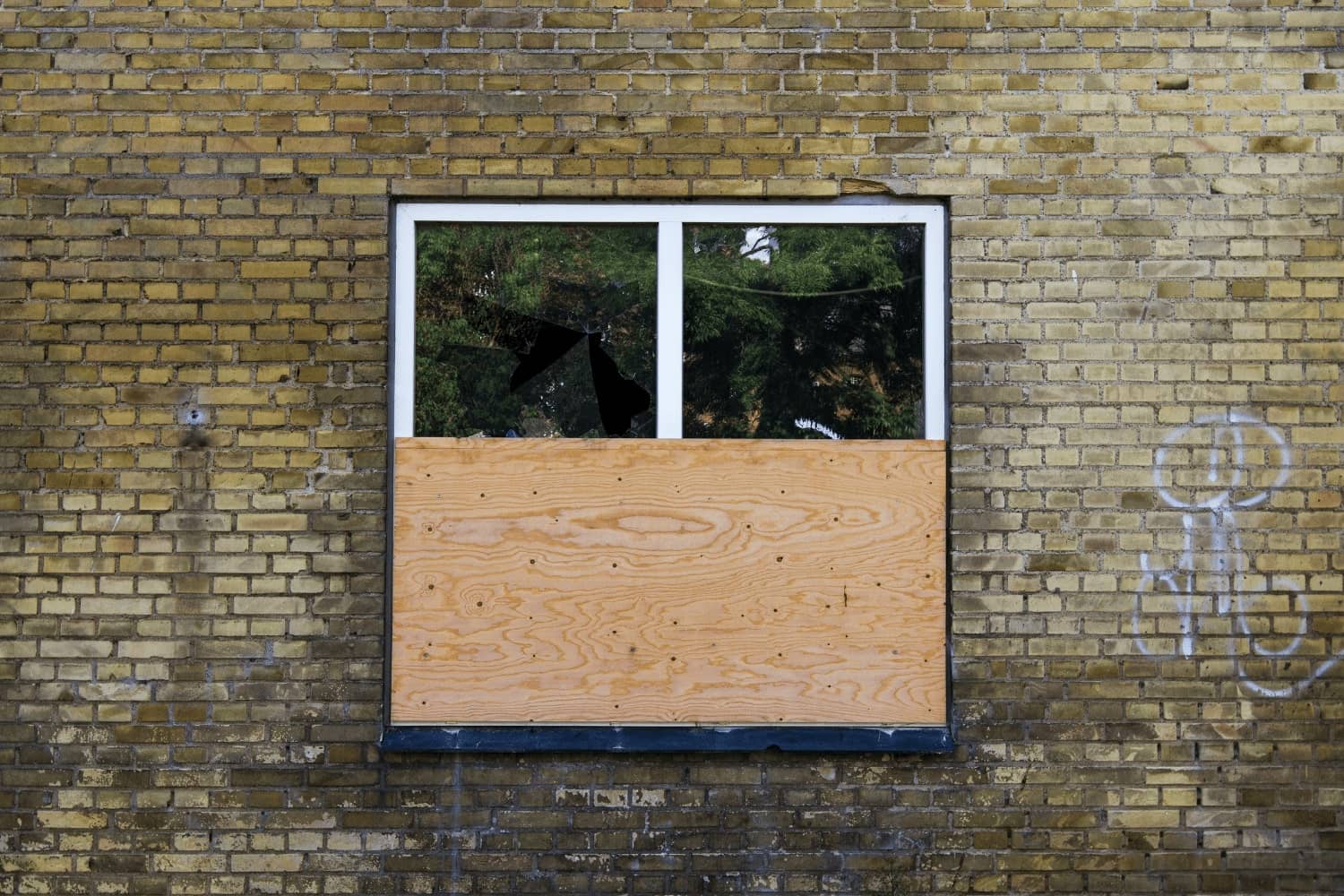 A brick wall with a window that has been boarded up
