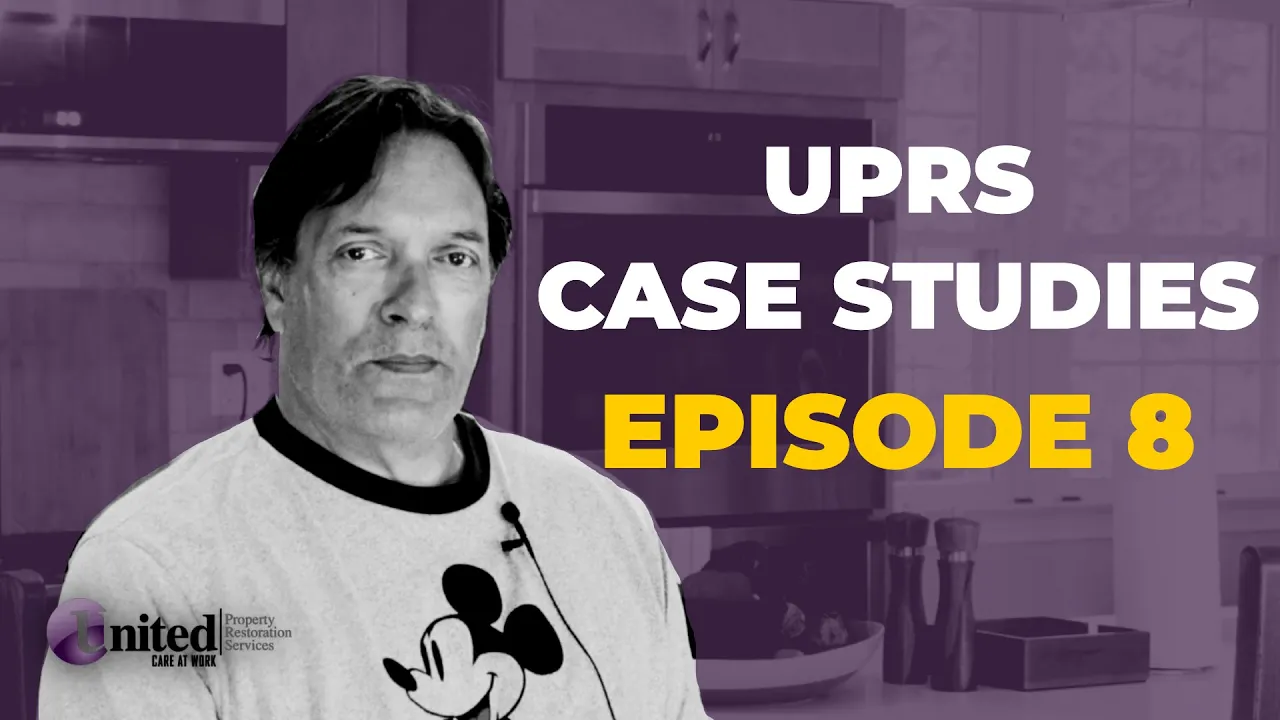 A man wearing a mickey mouse shirt is standing in a kitchen.