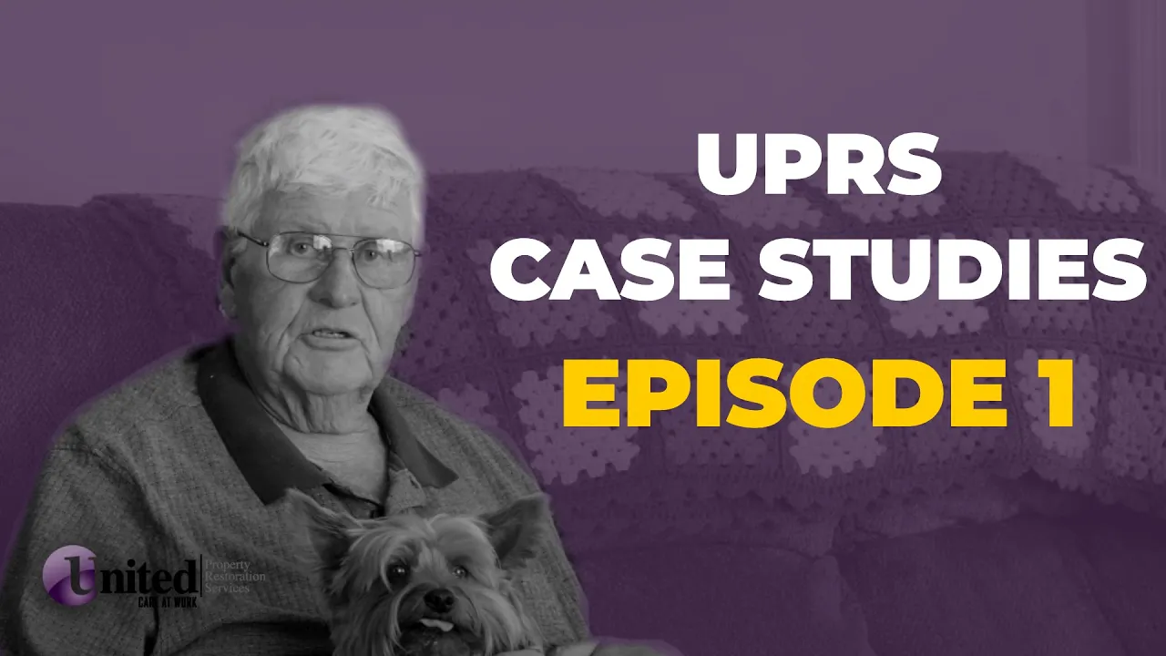 An older man is holding a dog in front of a purple background.