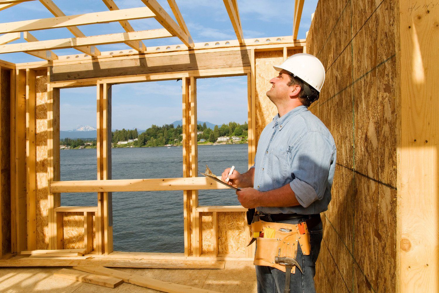 A man wearing a hard hat is standing in front of a building under construction