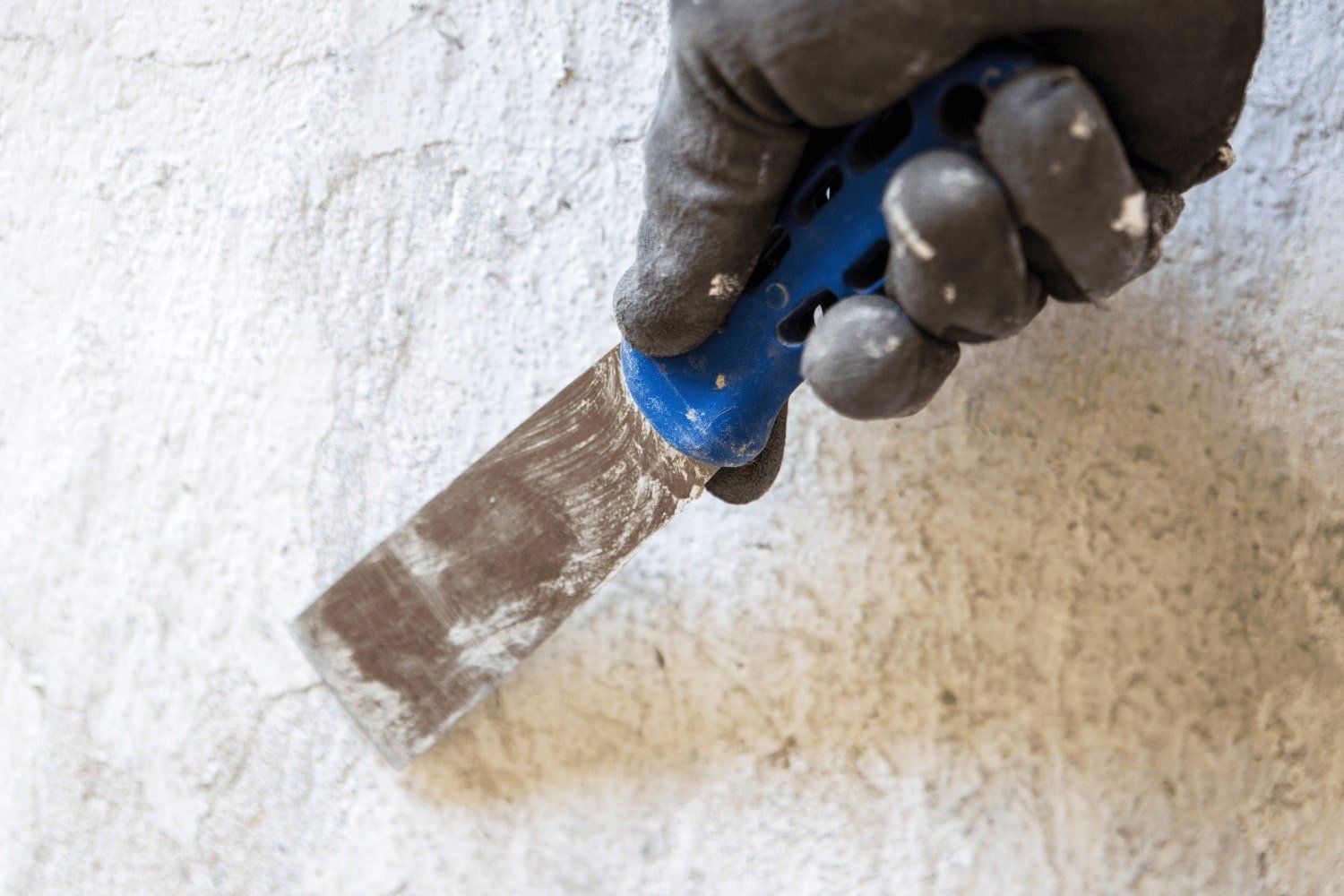 A person is holding a spatula over a white wall.