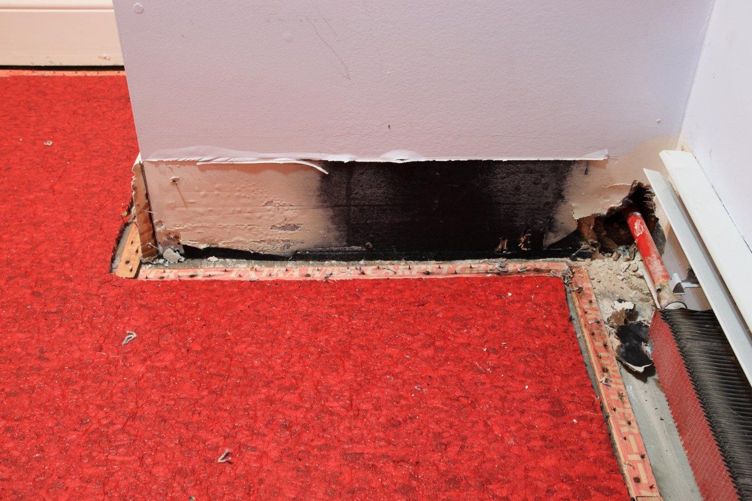 A red carpeted floor with a hole in the wall.