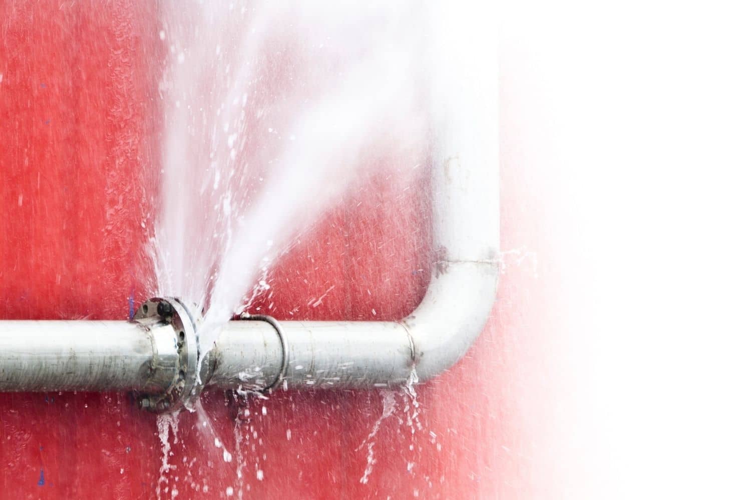 A pipe is leaking water on a red wall.