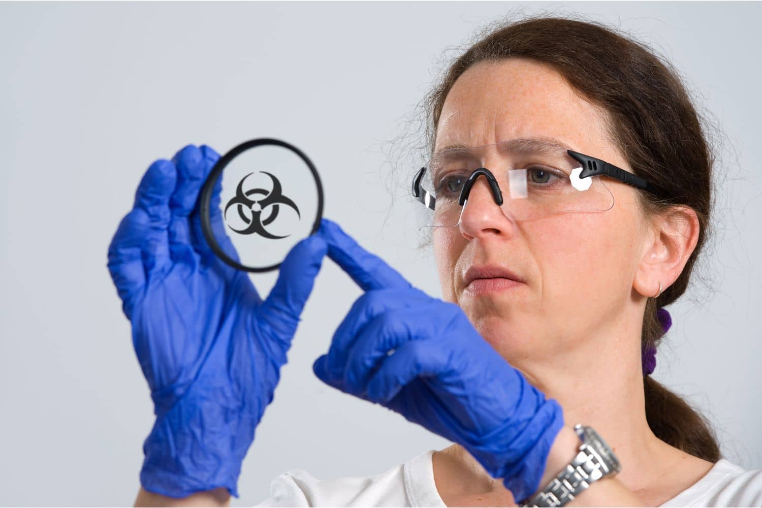 A woman wearing blue gloves is holding a glass with a biohazard symbol on it.