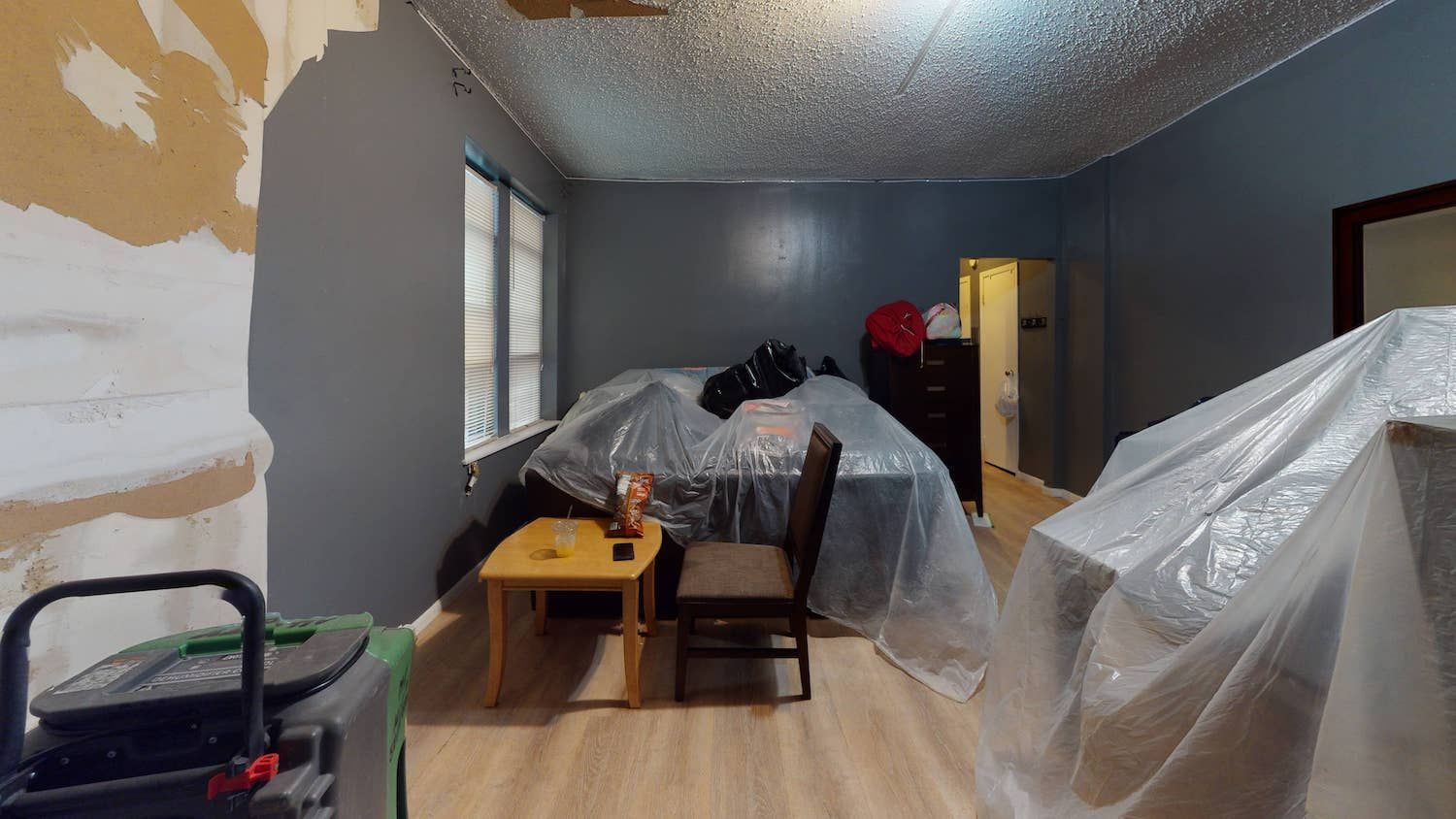 A room with a table , chairs , and a bed covered in plastic.