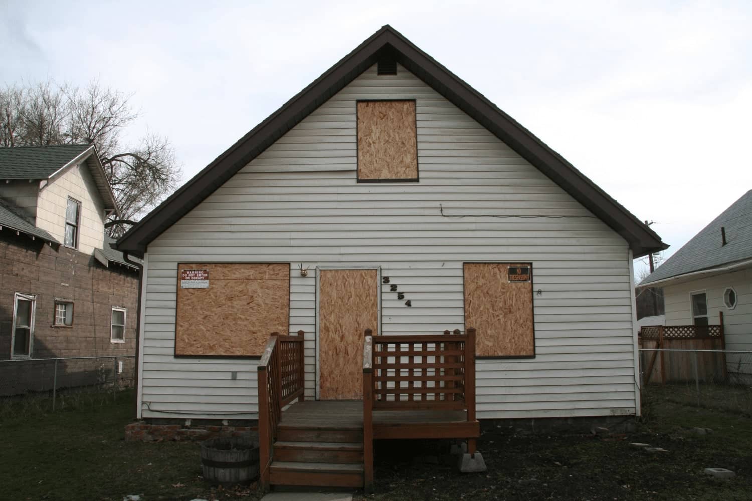 A white house with boarded up windows and a wooden deck