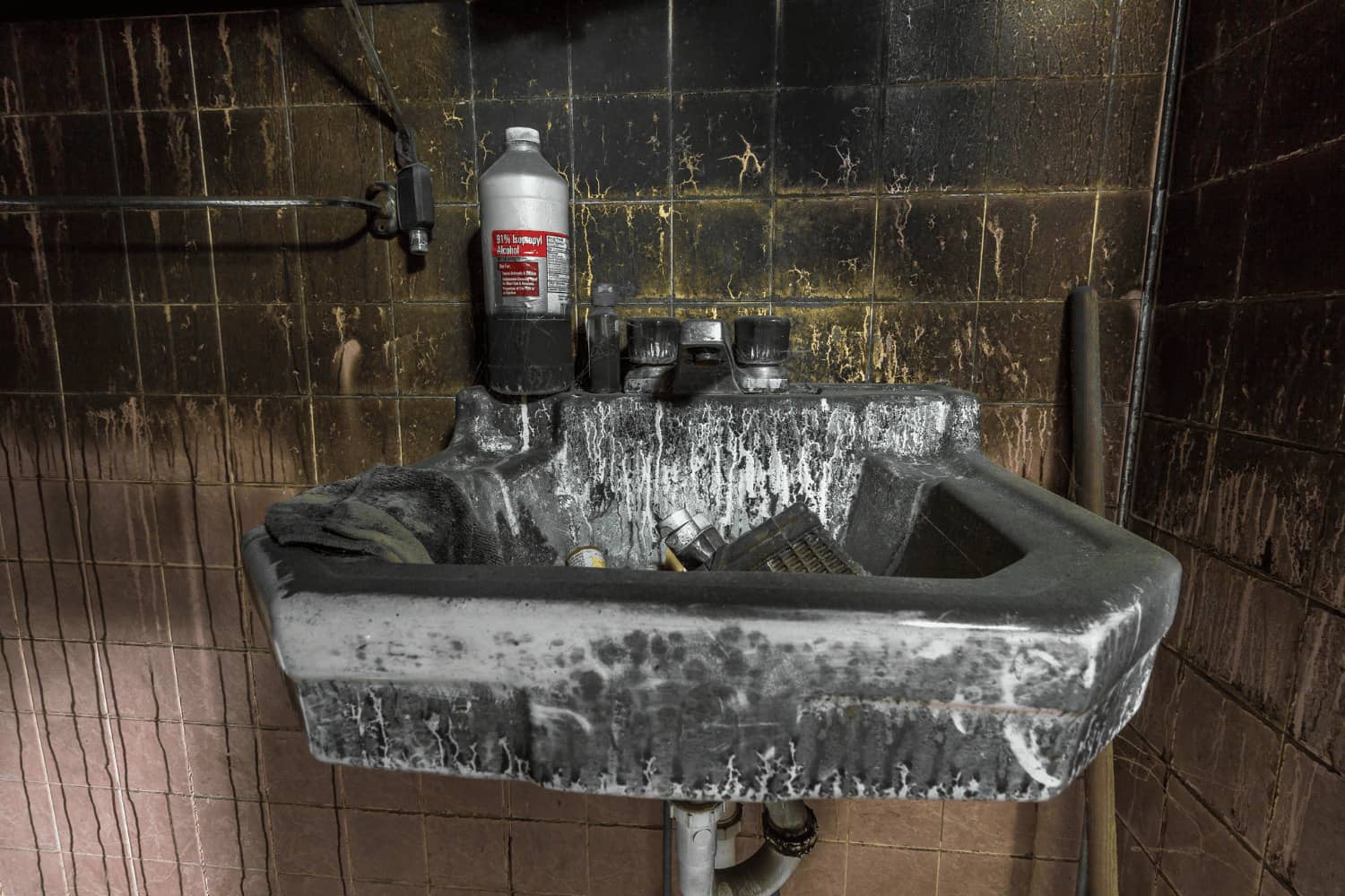 A dirty bathroom sink with a bottle of bleach on it.