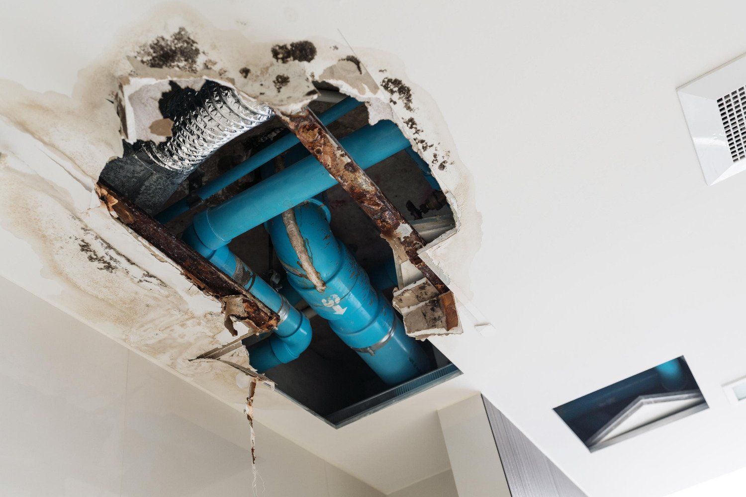 A hole in the ceiling with blue pipes coming out of it.