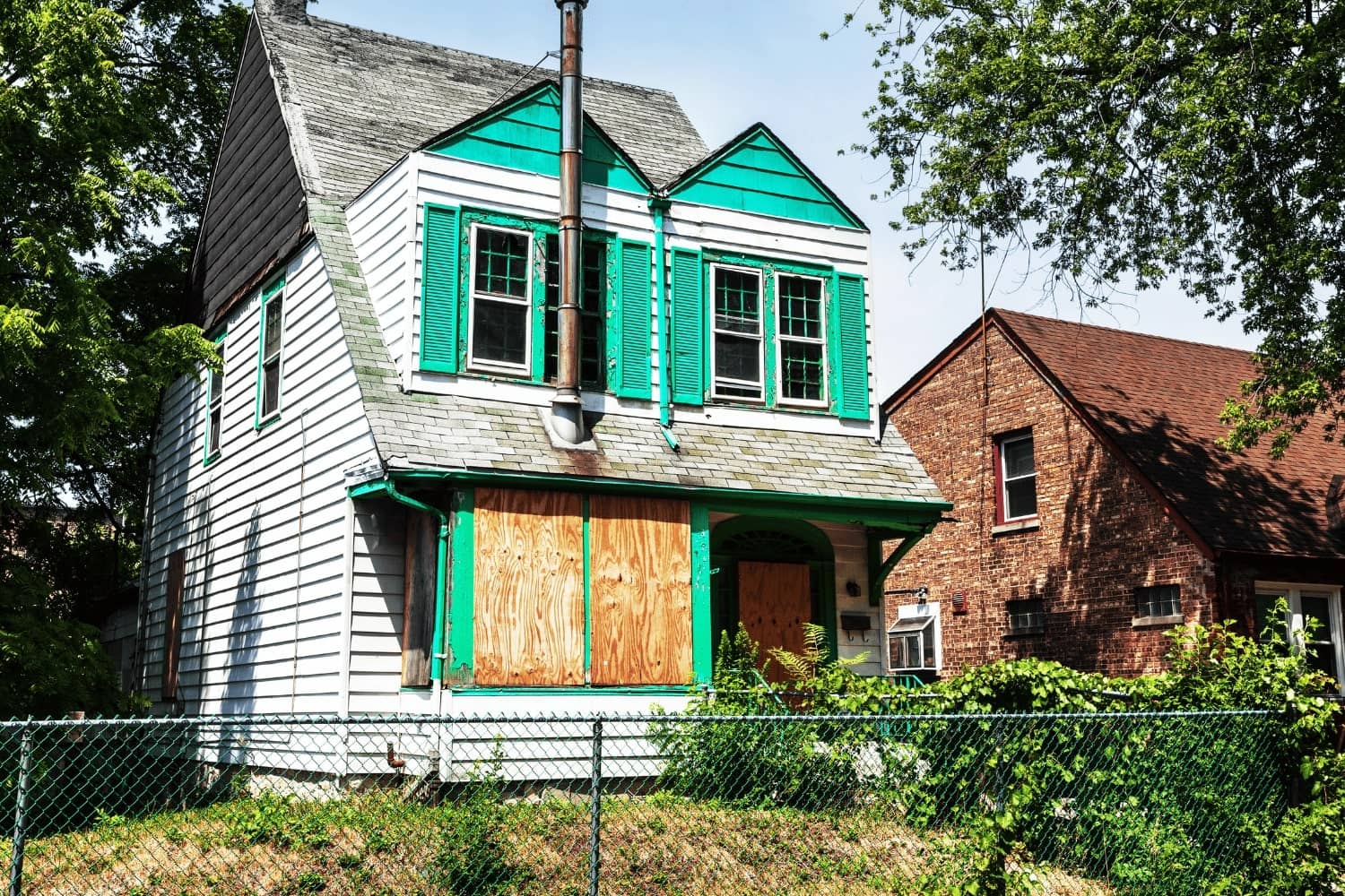A white house with green shutters and a brick house in the background.