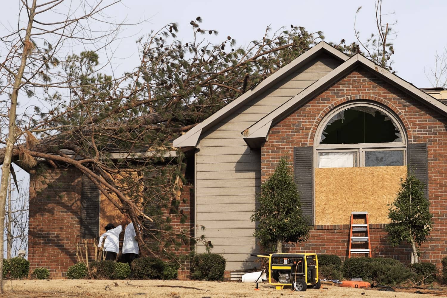 A house with a tree fallen on it and a generator in front of it.