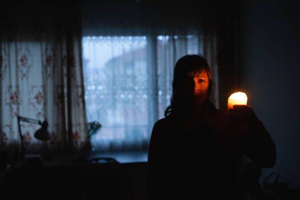 A woman is holding a candle in a dark room in front of a window.