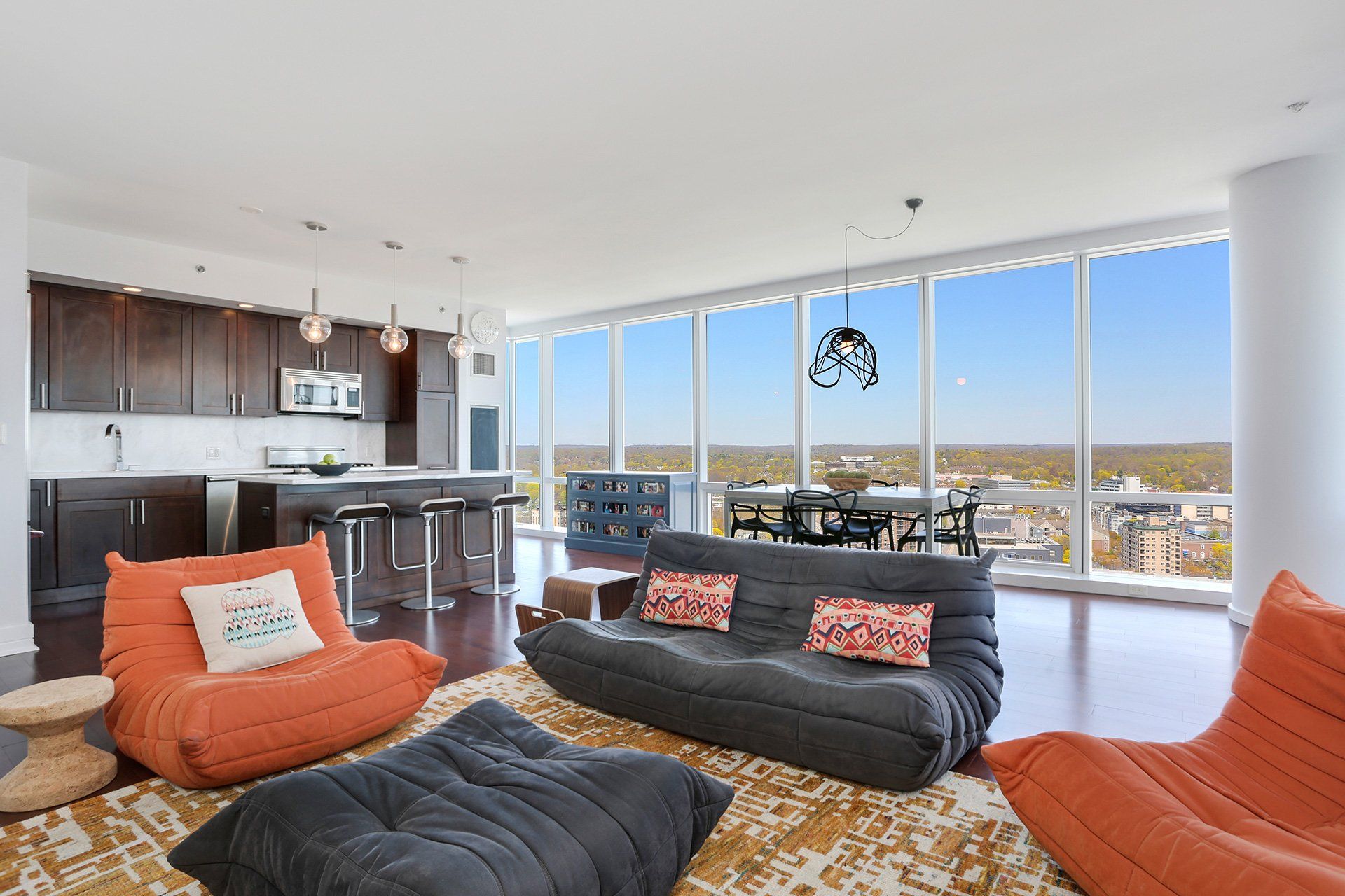 Modern living room with floor-to-ceiling windows, dark cabinets, and orange beanbag chairs.