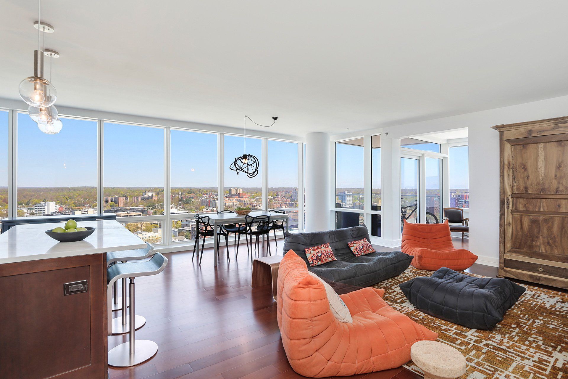 Modern living room with floor-to-ceiling windows, dark wood floor, beanbag chairs, and cityscape view.