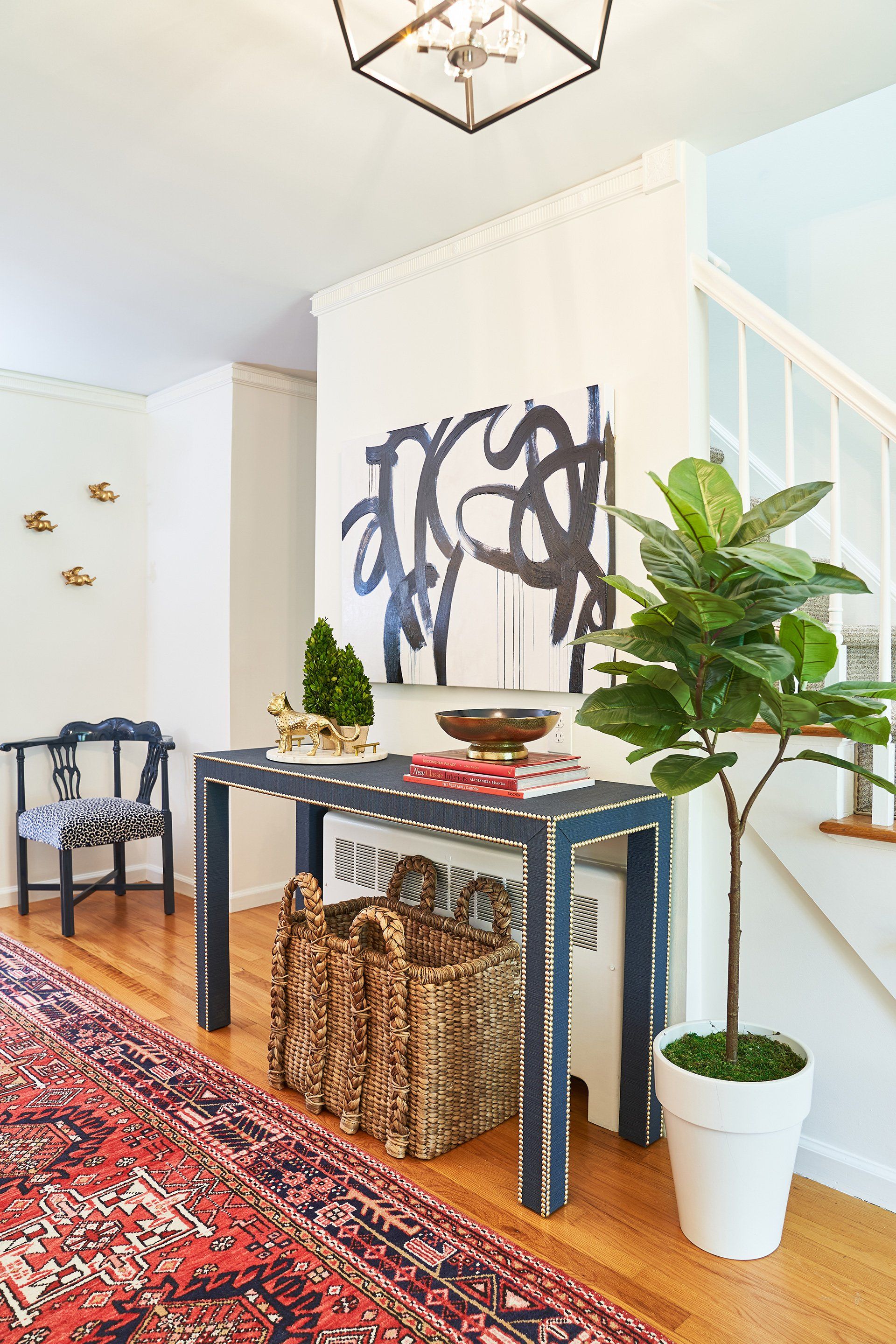 Hallway with a navy console table, artwork, a fiddle leaf fig, and a patterned rug.