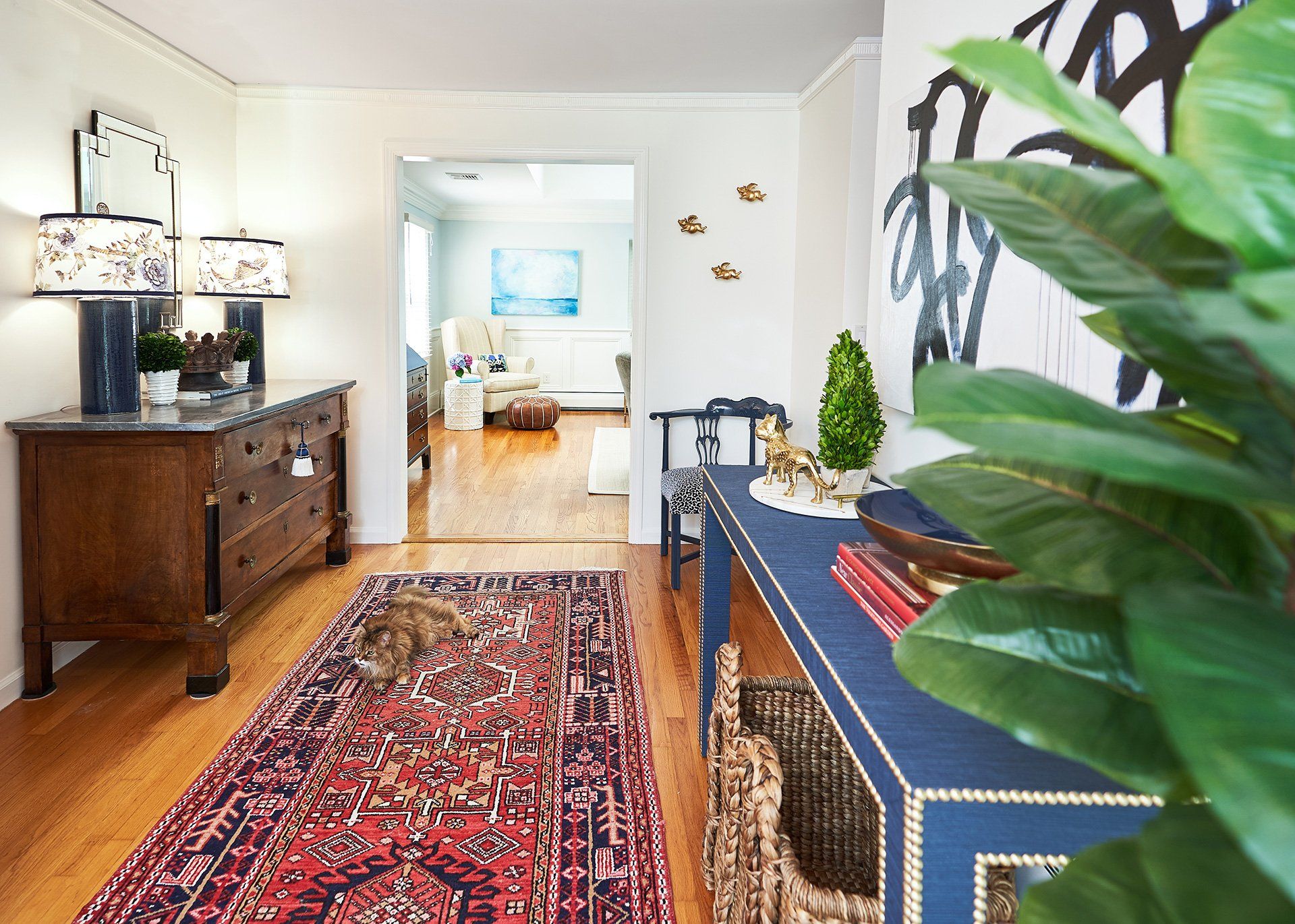 A hallway with wooden floors, a patterned rug, furniture, and a cat.