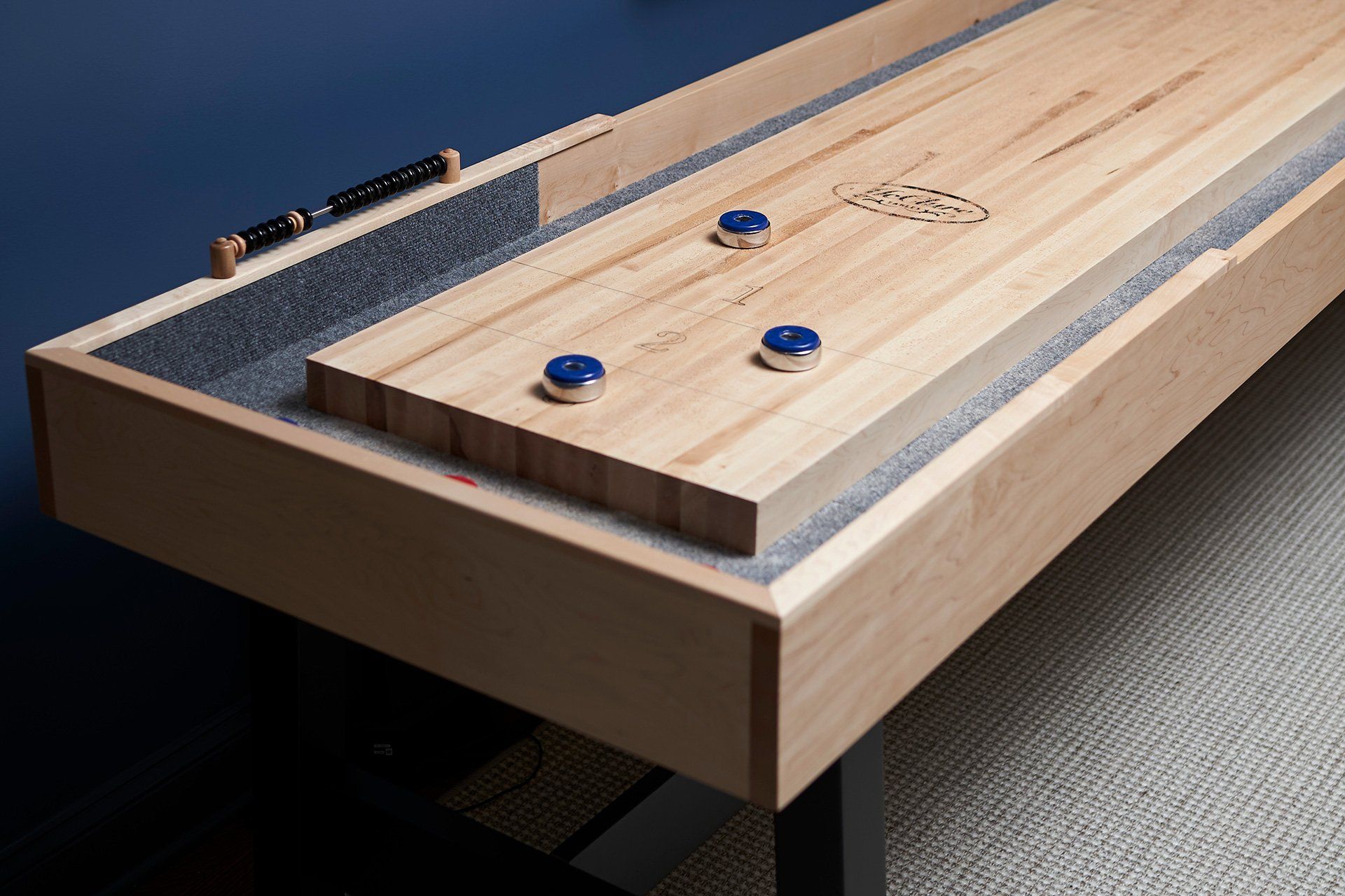 Shuffleboard table with three blue pucks, a black and gray surface, and wooden frame.