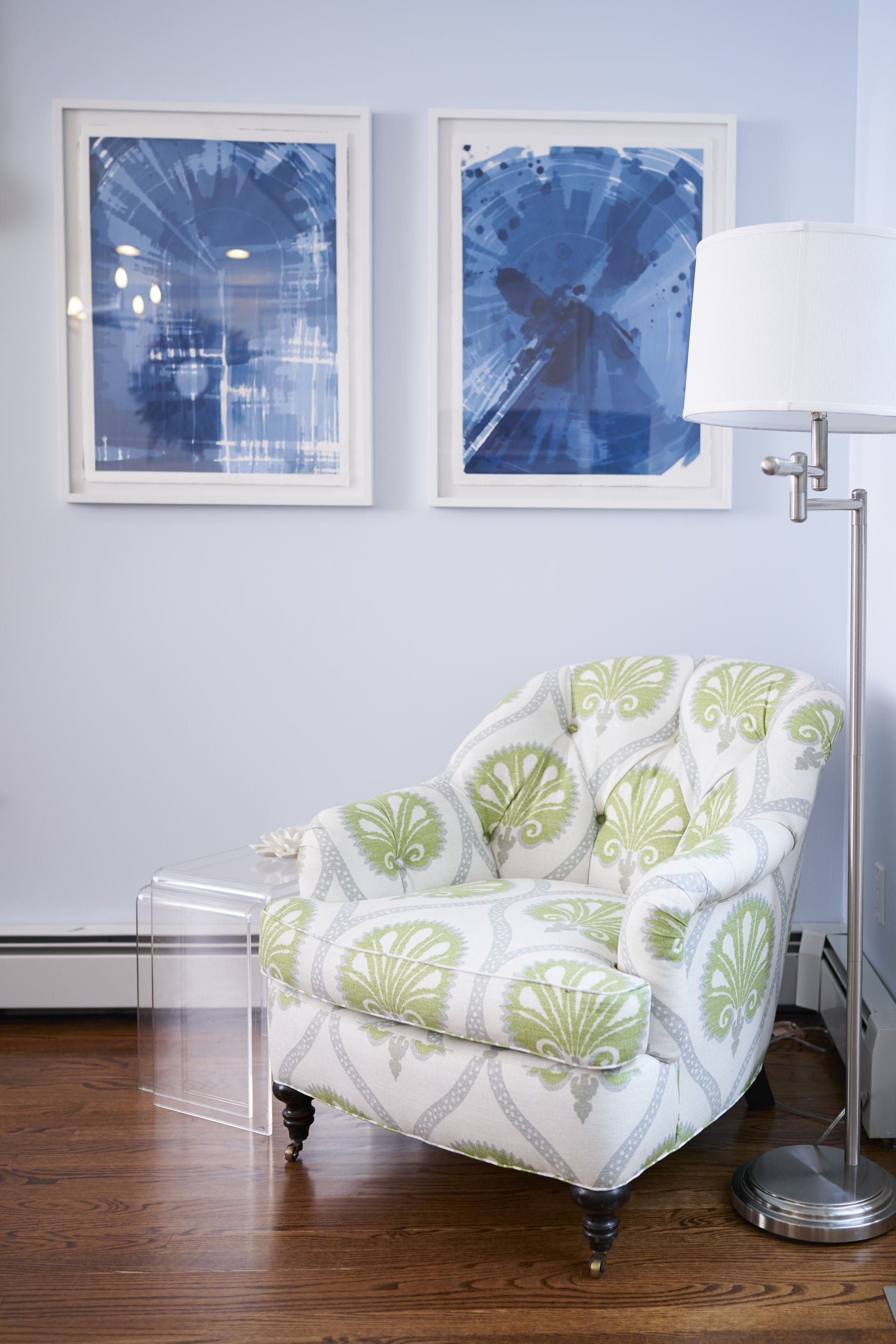 Tufted patterned armchair with blue art and silver lamp on wood floor.