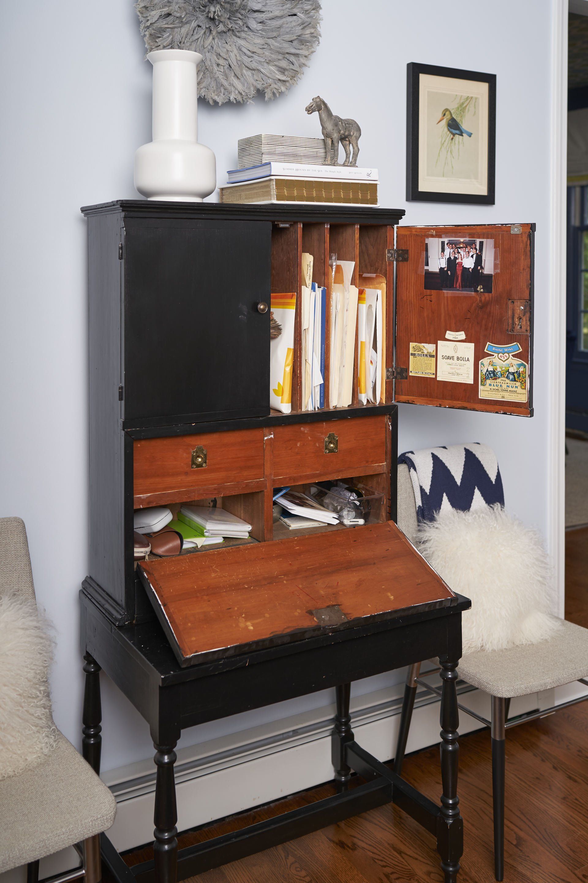 Black secretary desk with open drawers and cabinet, books and decor on top, blue wall background.