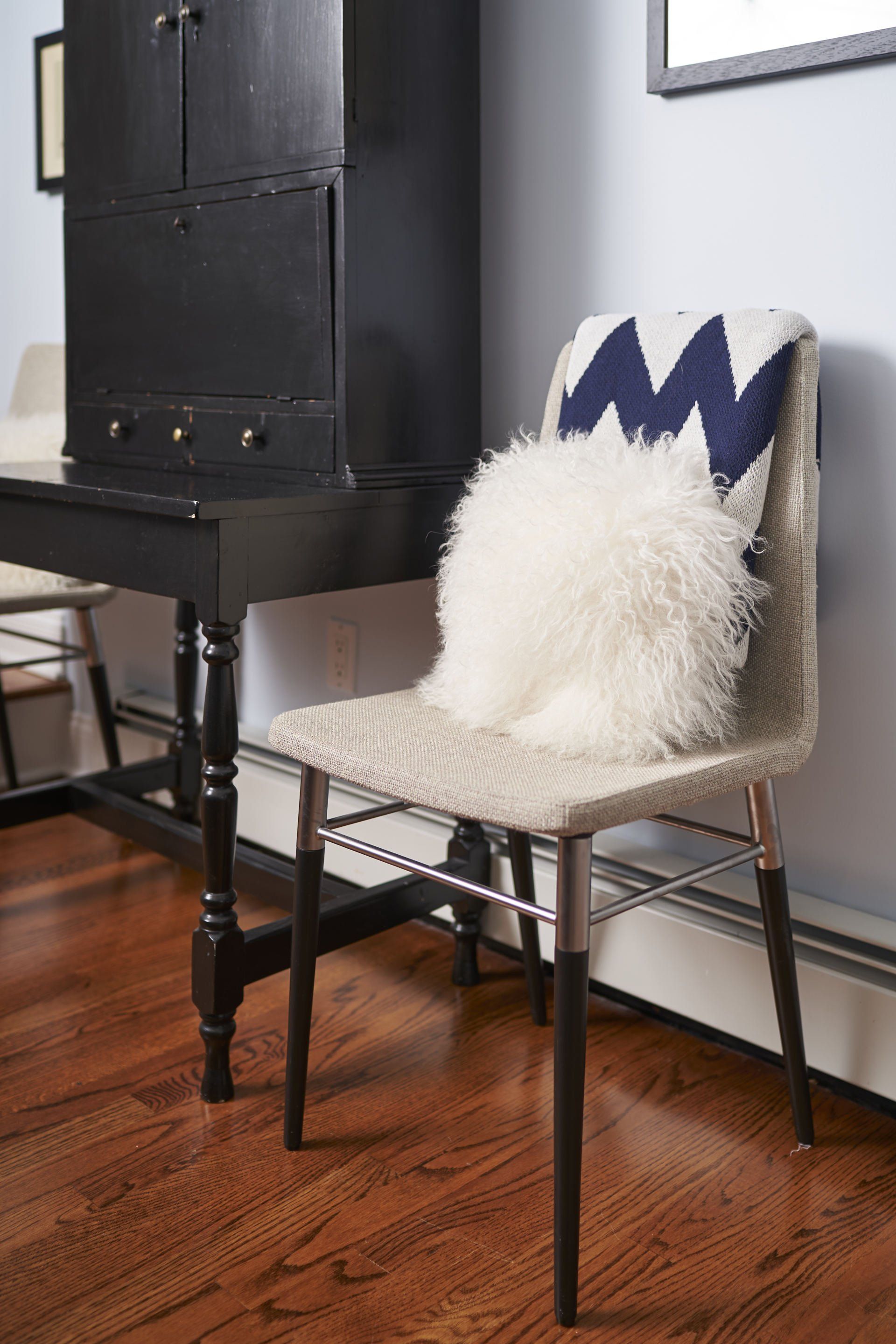 A chair with a white fur and blue zig-zag cushion next to a black cabinet.