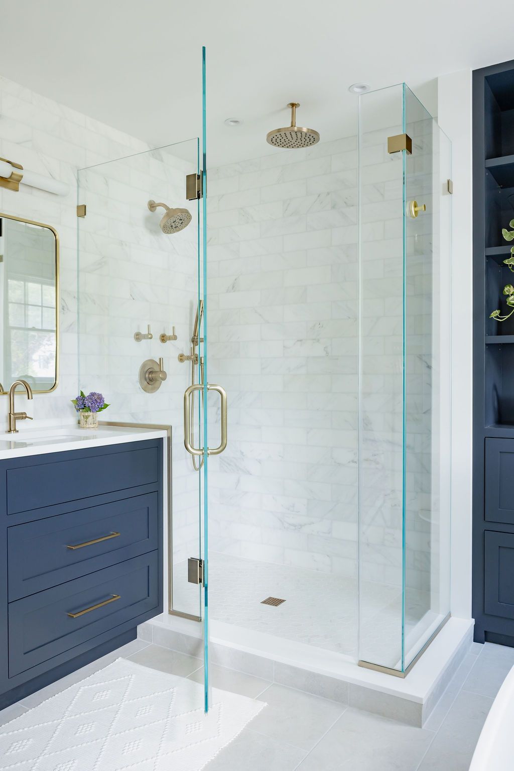 Bathroom with glass shower, marble tile, navy vanity, and gold fixtures.