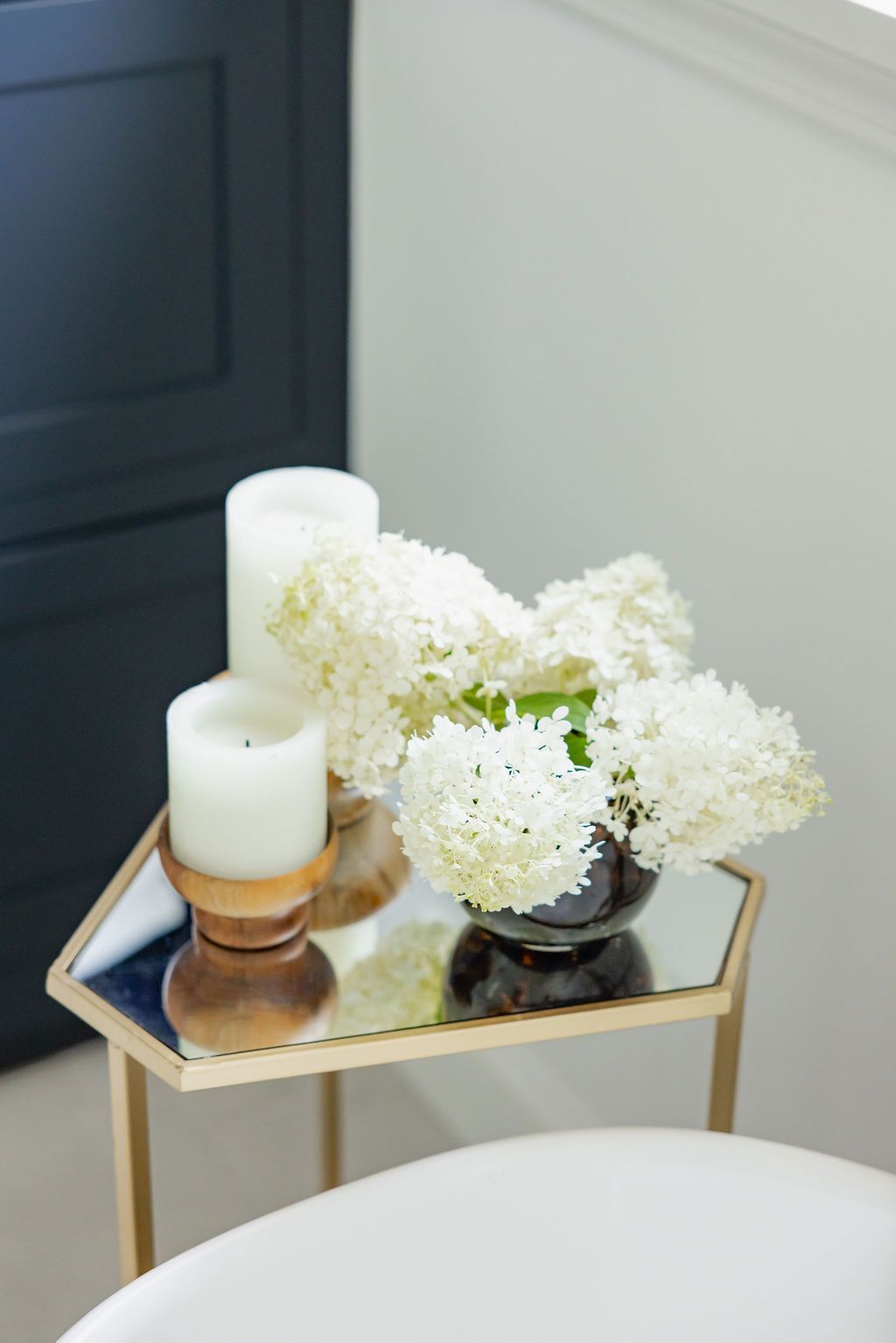A small table with a mirrored top holds white flowers in a vase, two candles, and gold legs.