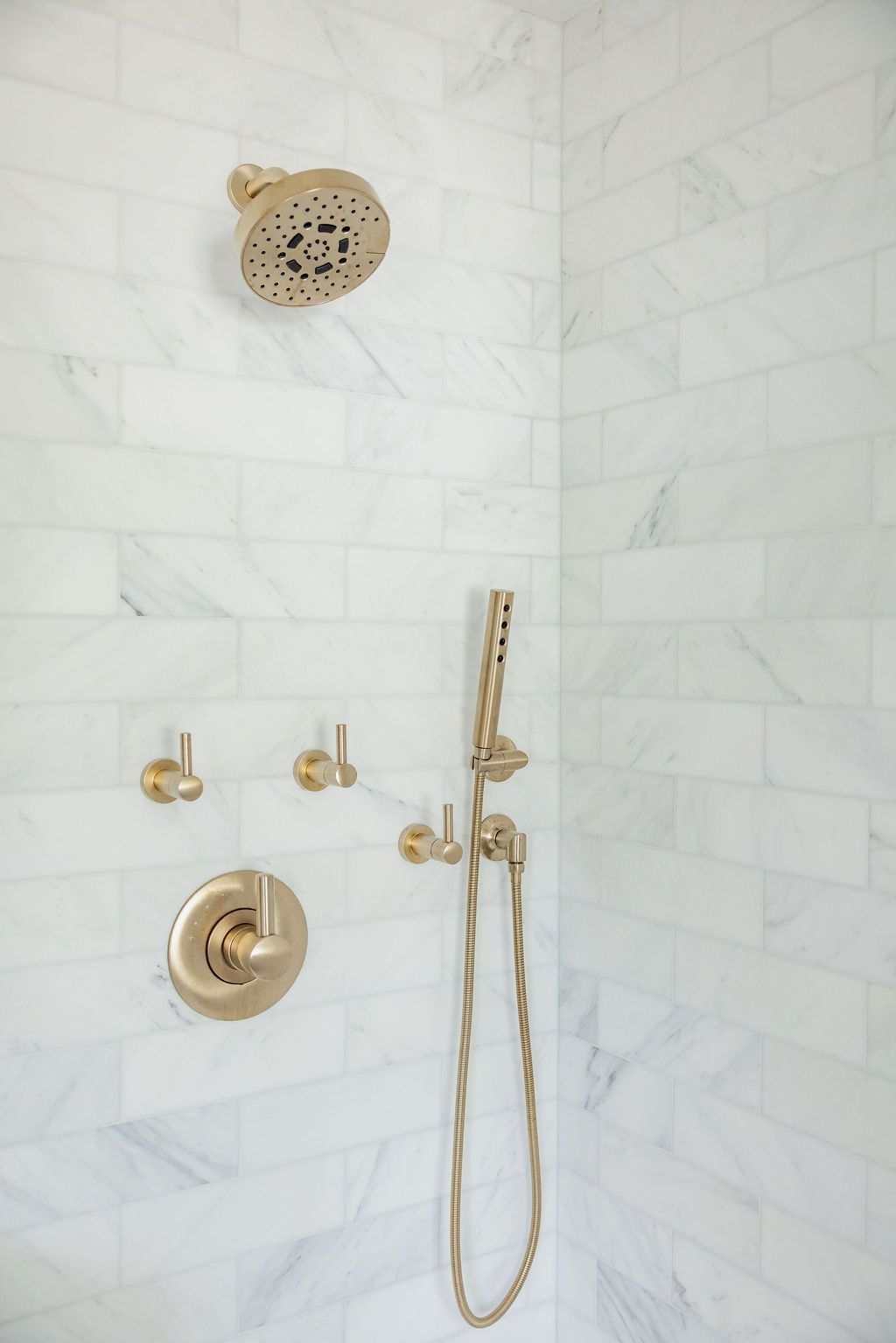 Gold shower fixtures against white marble subway tile in a bathroom.