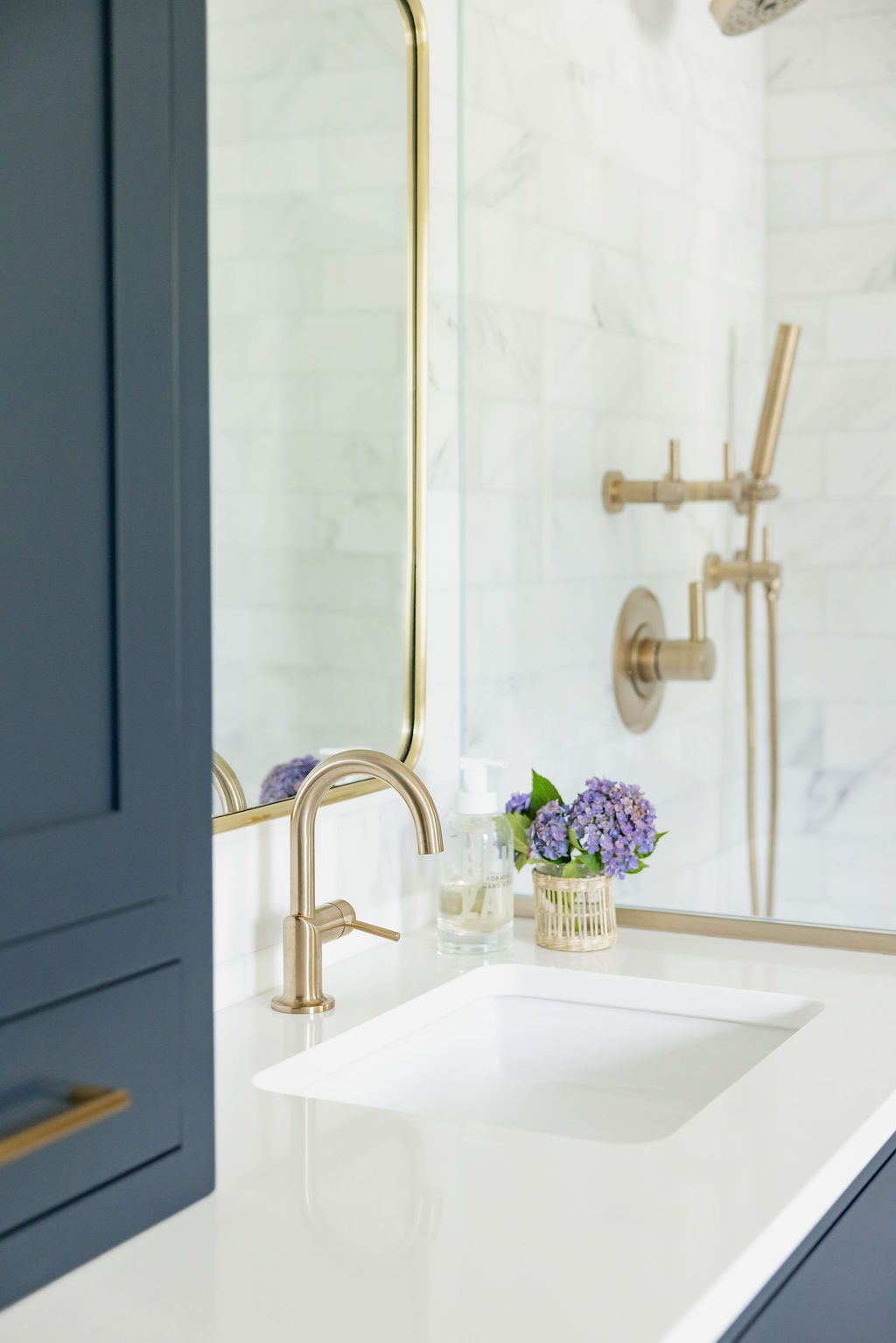 Bathroom with gold fixtures, white countertop, blue cabinet, and purple flowers.