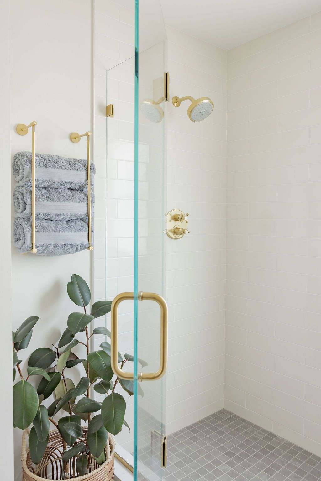 A bright, modern bathroom with a glass shower and gold fixtures. Plant in a basket near towels.