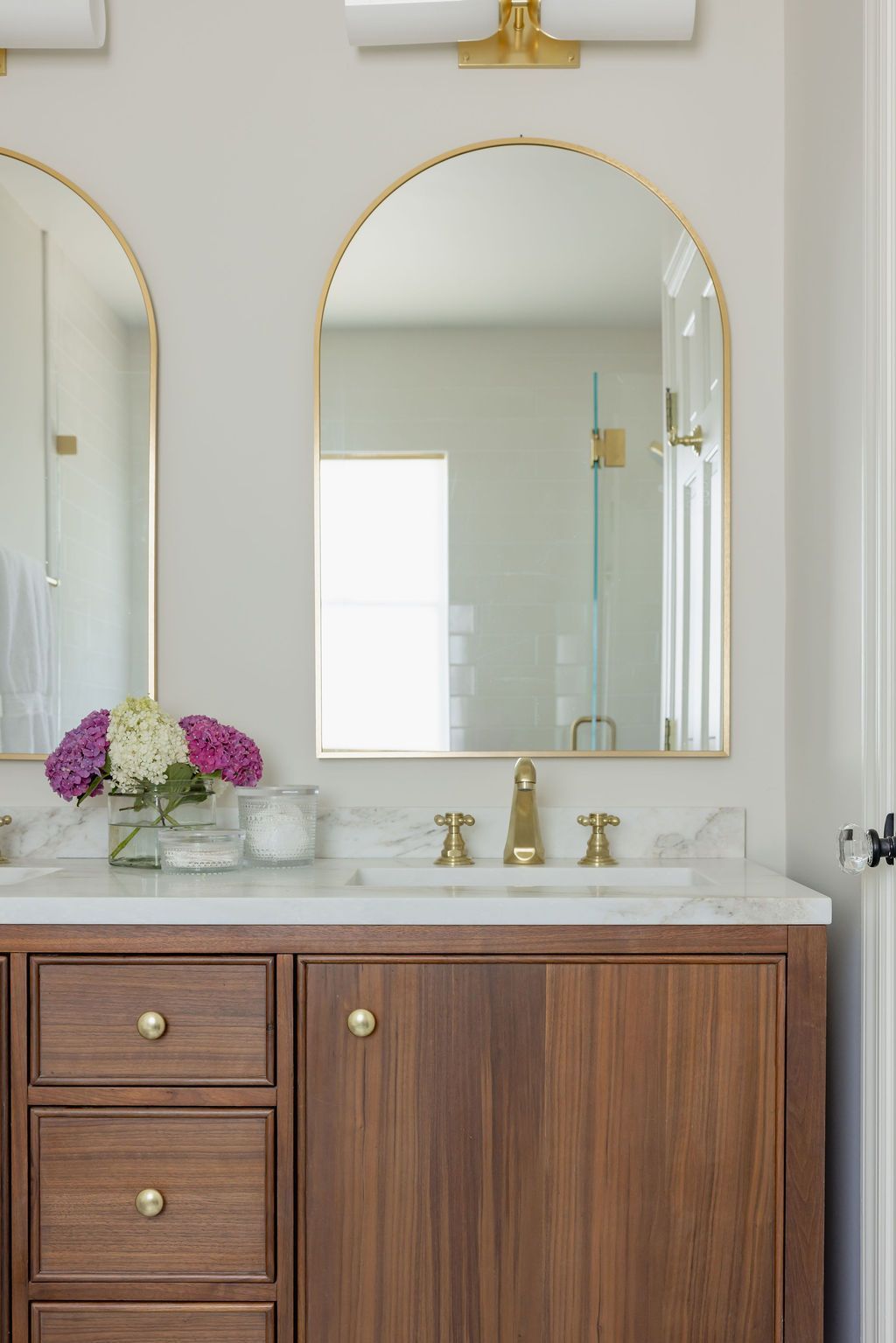 Bathroom vanity with arched gold-framed mirror, wood cabinets, and marble countertop.