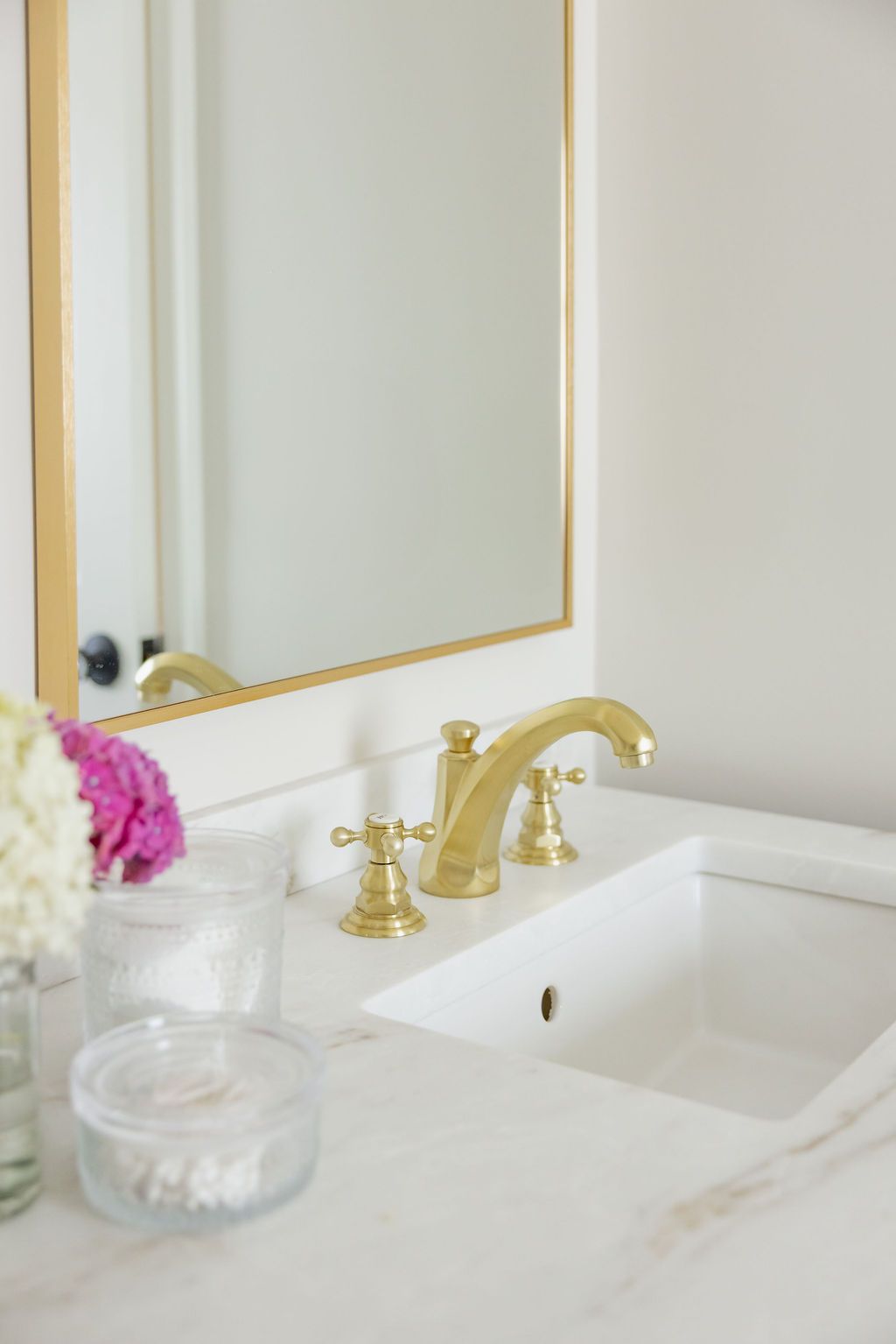 Gold faucet and fixtures on a white marble sink in a bathroom, framed mirror.