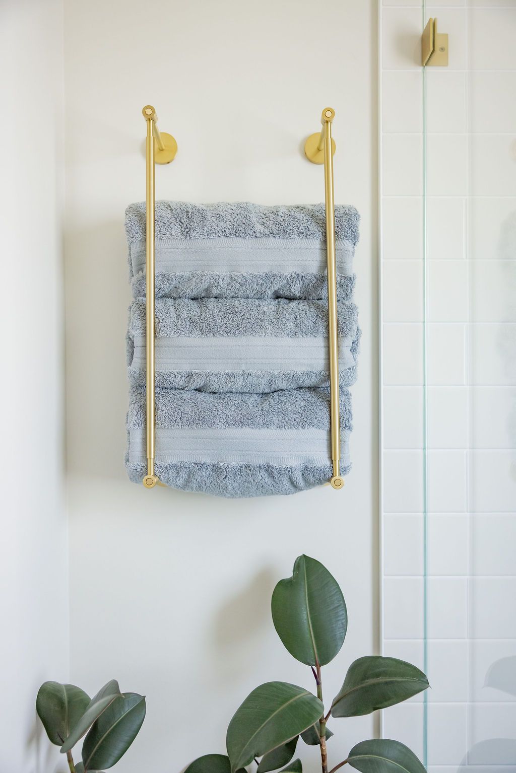 Towel rack with a blue and gray towel on a white wall. Green plants in foreground.