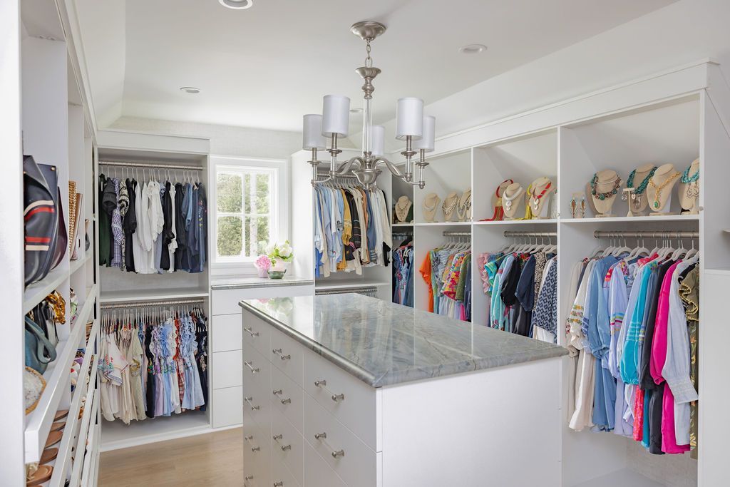 Walk-in closet with white shelves and clothing racks. A center island has a granite countertop. A chandelier hangs from the ceiling.