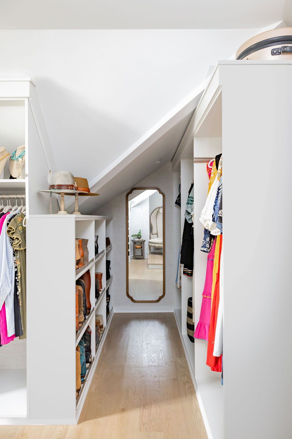Narrow walk-in closet with white shelving, a mirror, and clothes hanging.