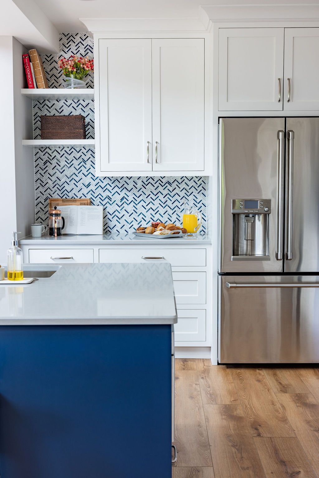 Kitchen with blue island, white cabinets, stainless steel refrigerator, and mosaic backsplash.